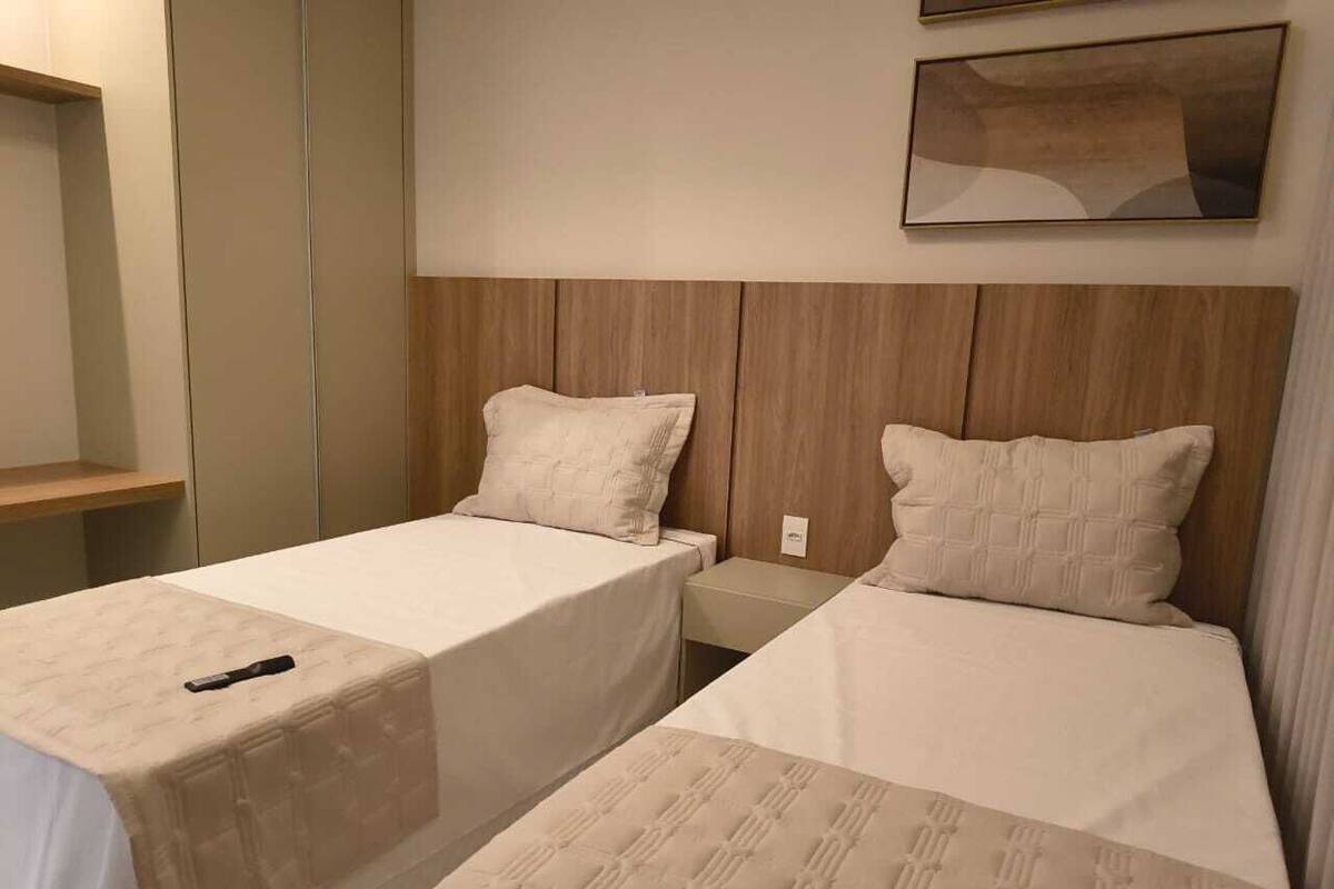 Una habitación de hotel con dos camas individuales, cabecero de madera, mesita de noche y una obra de arte colgada en la pared.