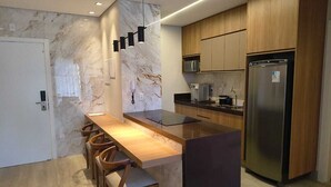 Una cocina moderna con protector contra salpicaduras de mármol, armarios de madera, un refrigerador de acero inoxidable y una larga mesa de comedor con sillas.