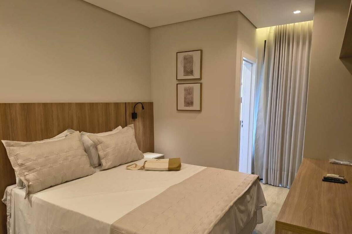 Una habitación de hotel con una cama, una mesita de noche, una lámpara y una puerta con cortinas.