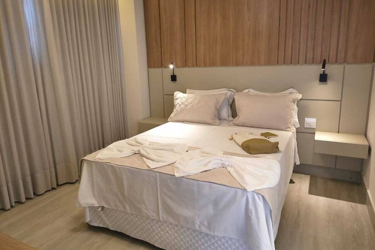 Un dormitorio con cama, cortinas, mesita de noche y lámpara en la pared.