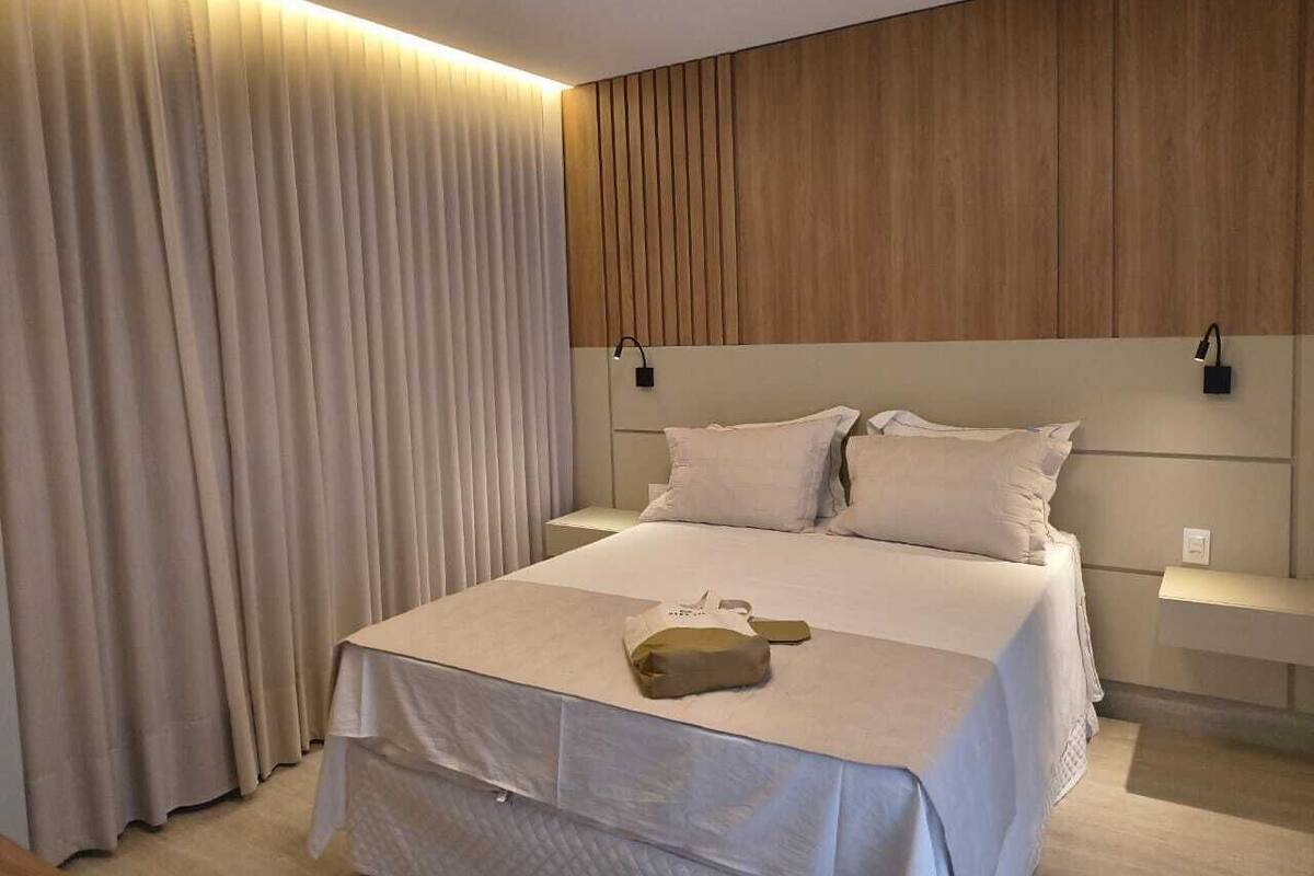 Una habitación de hotel moderna con una cama grande, una mesita de noche, una lámpara de pared y una cortina.