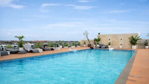 Ein Pool auf dem Dach mit Liegestühlen, Topfpflanzen und Blick auf die Stadtlandschaft.