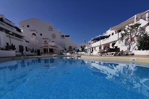 Ein klarer, blauer Pool, umgeben von weißen Gebäuden mit Balkonen und wolkenlosem Himmel.