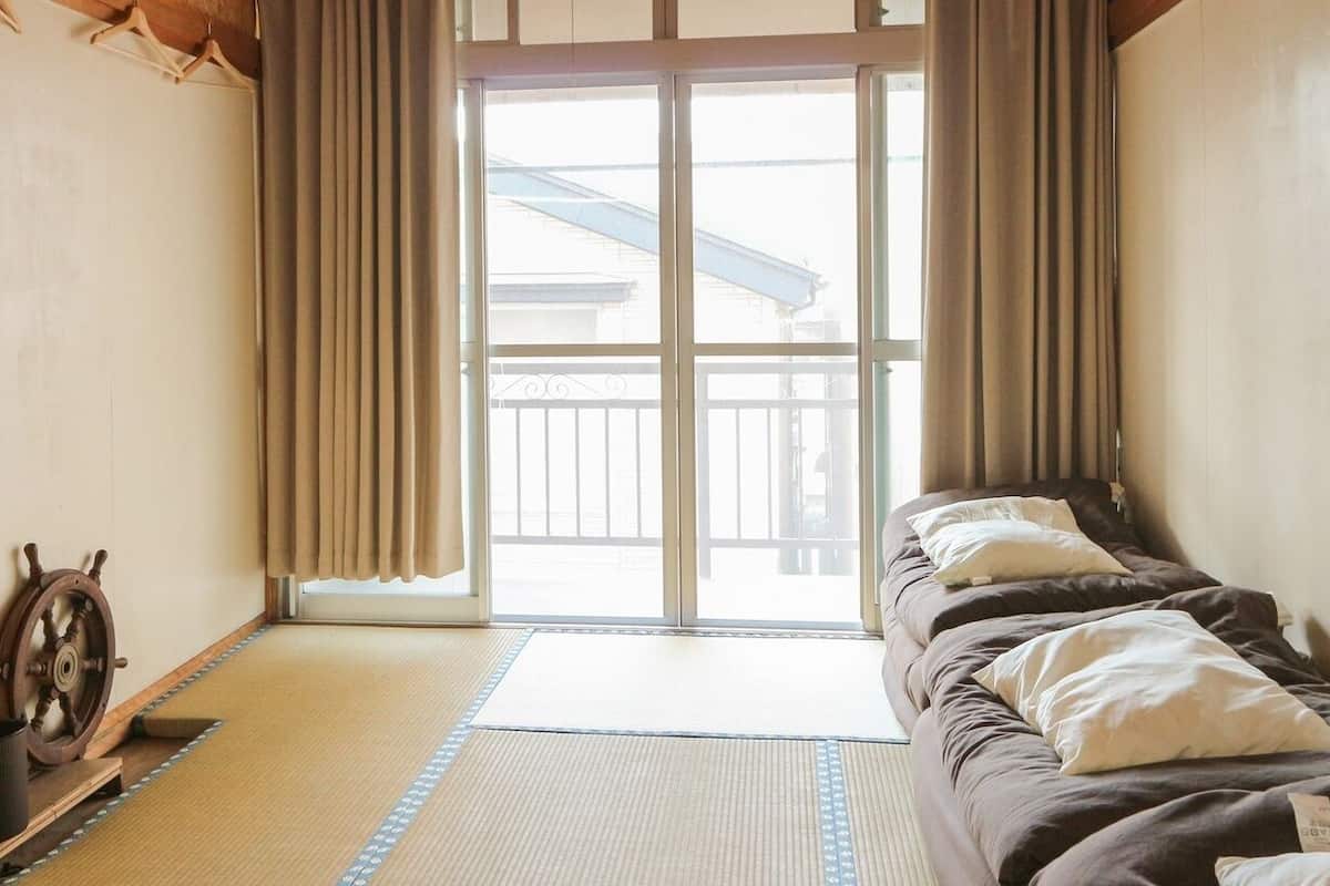 A room with a bed, a mat, a wooden ship wheel, and a view of a balcony.