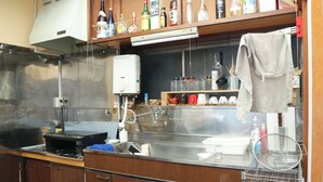 A kitchen with a stainless steel sink, a stove, and various bottles on a shelf.