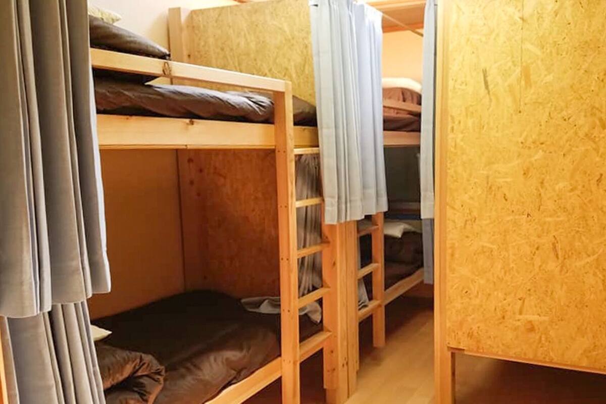A bunk bed room with a wooden floor, a small wooden cabinet, and a curtain.