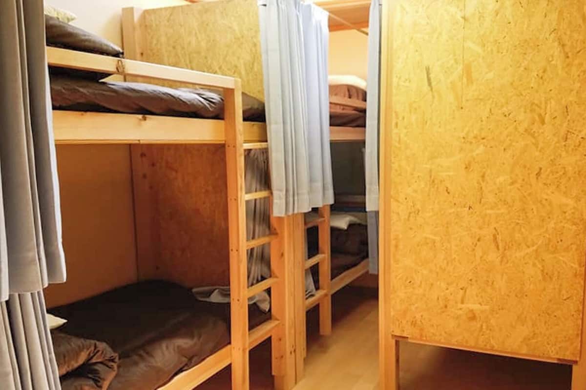 A bunk bed room with a wooden bunk bed, a lower bunk with a mattress, and a small wooden cabinet.