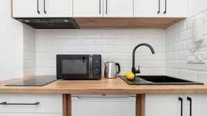 Een keuken met witte kastjes, een zwarte magnetron, een waterkoker, een spoelbak en een citroen op het aanrecht.
