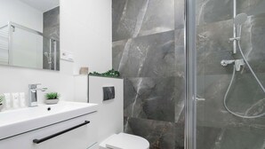 Een moderne badkamer met een glazen douchecabine, een witte wastafel en een toilet.