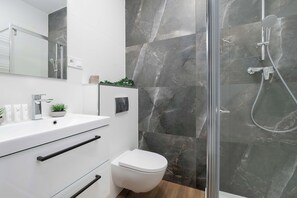 Ein modernes Badezimmer mit einer gläsernen Duschkabine, einem weißen Waschbecken und einer Toilette.