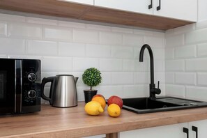 Eine Küche mit Mikrowelle, Wasserkocher, Spüle und Obst auf der Arbeitsfläche.