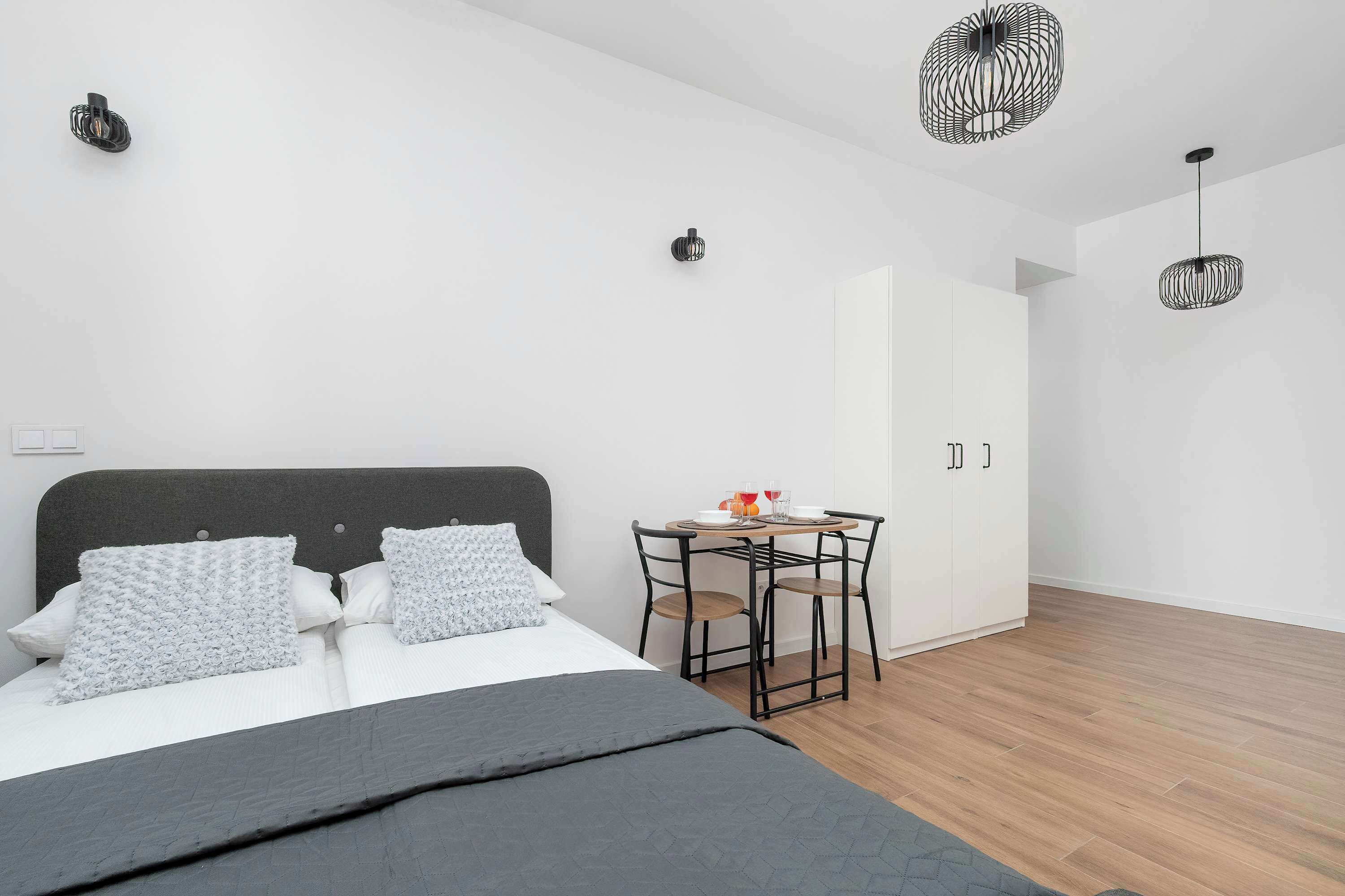 Un dormitorio moderno con cama, mesitas de noche, un escritorio y dos lámparas colgantes.