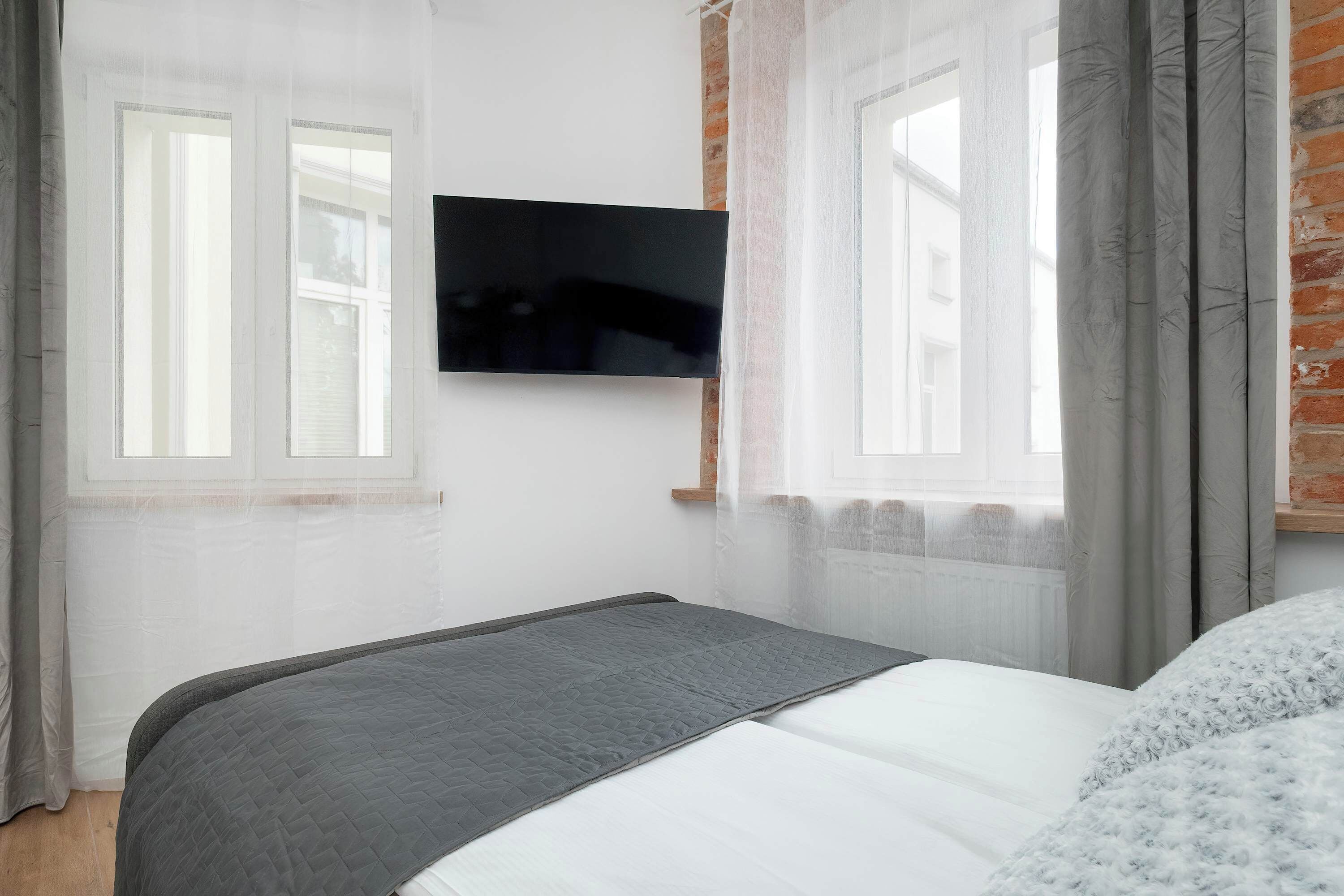 Un dormitorio con cama, televisor montado en la pared y ventanas con cortinas.