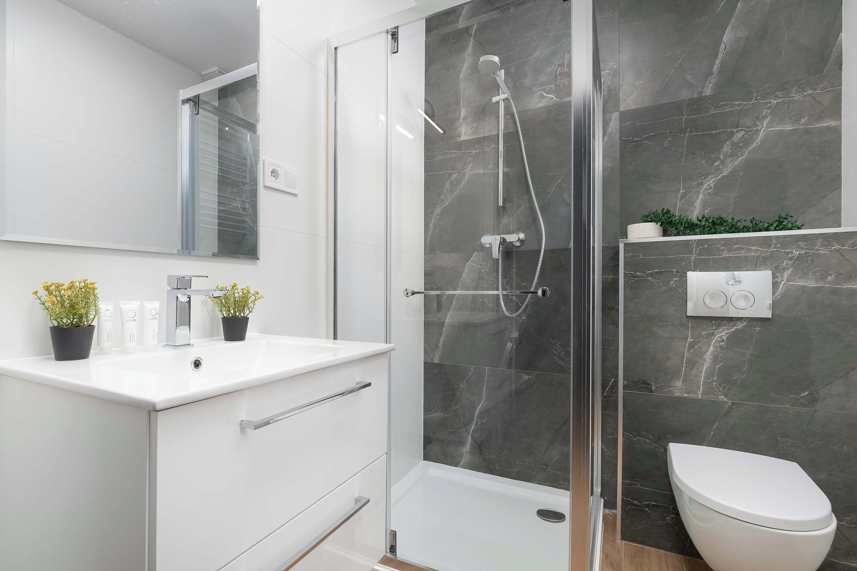 Un baño moderno con cabina de ducha de vidrio, un lavamanos blanco con espejo y un inodoro.
