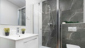 Ein modernes Badezimmer mit einer Duschkabine, einem weißen Waschbecken mit Spiegel und einer Toilette.