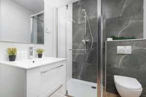 Ein modernes Badezimmer mit einer Duschkabine, einem weißen Waschbecken mit Spiegel und einer Toilette.