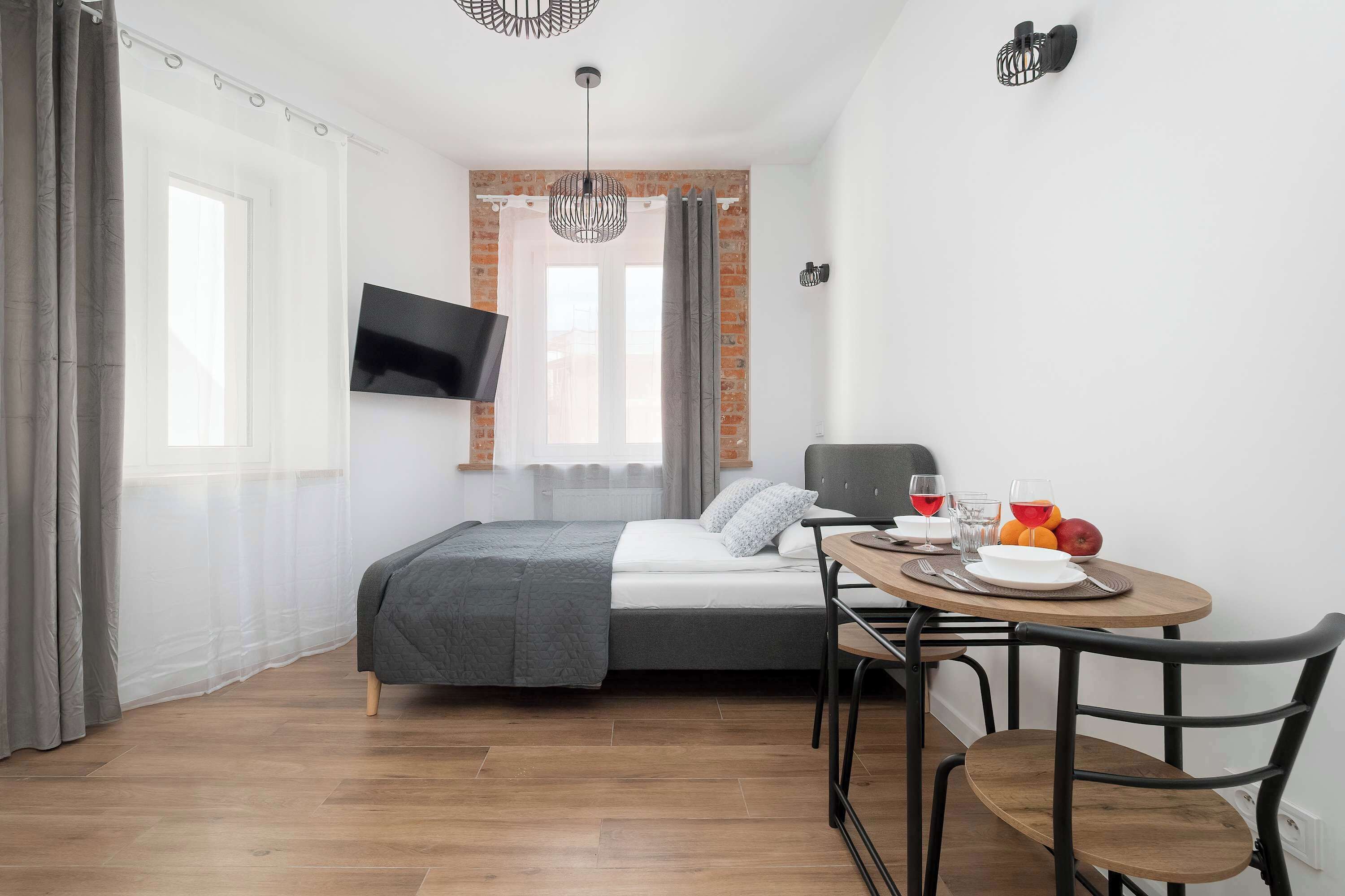 Una camera da letto con un letto, una TV fissata al muro, un tavolo da pranzo con sedie e un angolo per la colazione.