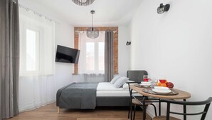 Ein Schlafzimmer mit einem Bett, einem an der Wand montierten Fernseher, einem Esstisch mit Stühlen und einer Frühstücksecke.