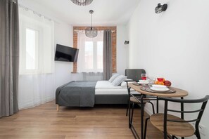 Ein Schlafzimmer mit einem Bett, einem an der Wand montierten Fernseher, einem Esstisch mit Stühlen und einer Frühstücksecke.
