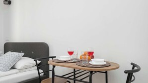 Ein Bett mit grauem Kopfteil, ein Nachttisch mit zwei Gläsern roter Flüssigkeit, eine Schale und ein Teller.