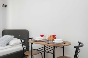 Ein Bett mit grauem Kopfteil, ein Nachttisch mit zwei Gläsern roter Flüssigkeit, eine Schale und ein Teller.