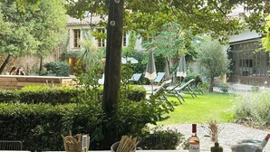 An outdoor dining area with a table set for a meal, surrounded by greenery and a view of a courtyard. - Historic house in the heart of Provence (Brignoles)
