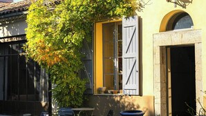 A building with a yellow facade, shutters, a door, and a window. There is a tree with green leaves in front of the building. - Historic house in the heart of Provence (Brignoles)
