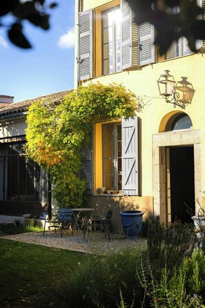 A building with a yellow facade, shutters, a door, and a window. There is a tree with green leaves in front of the building. - Historic house in the heart of Provence (Brignoles)