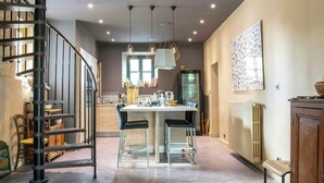 A modern kitchen with a central island, a spiral staircase, and pendant lighting. - Historic house in the heart of Provence (Brignoles)