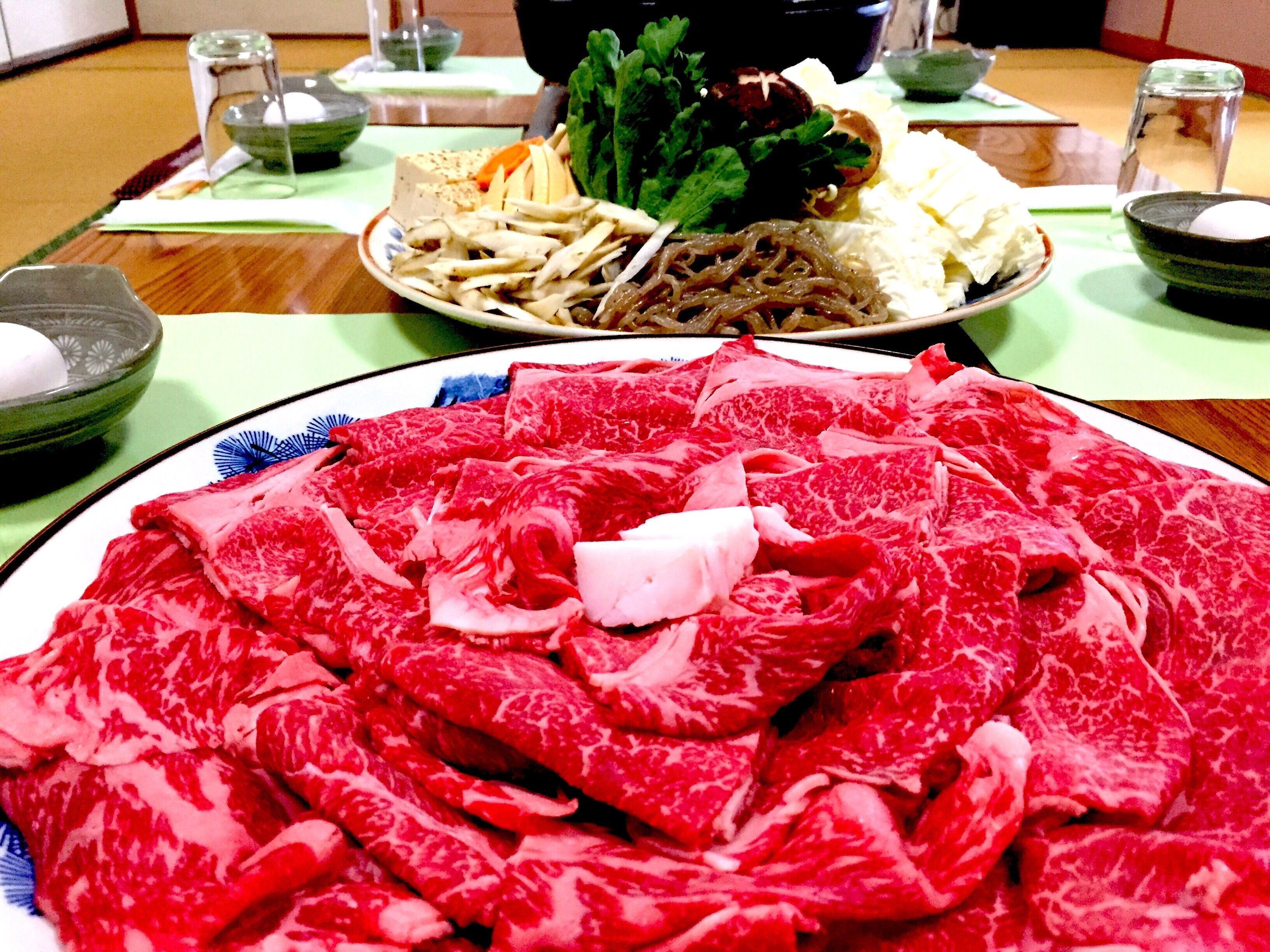A table with various food items, including sliced meat, vegetables, and a bowl of soup.