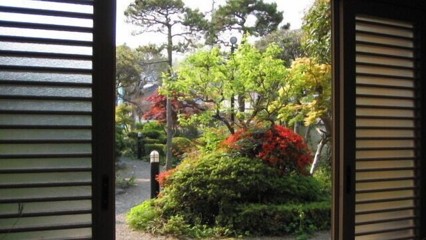 A view through a door with a garden outside, featuring various trees and shrubs. - Nadaya Ryokan (Mimasaka)