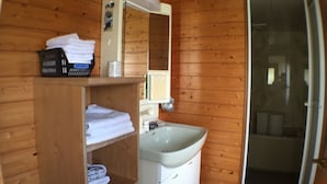A wooden cabin bathroom with a sink, mirror, and shelves with towels. - Nadaya Ryokan (Mimasaka)