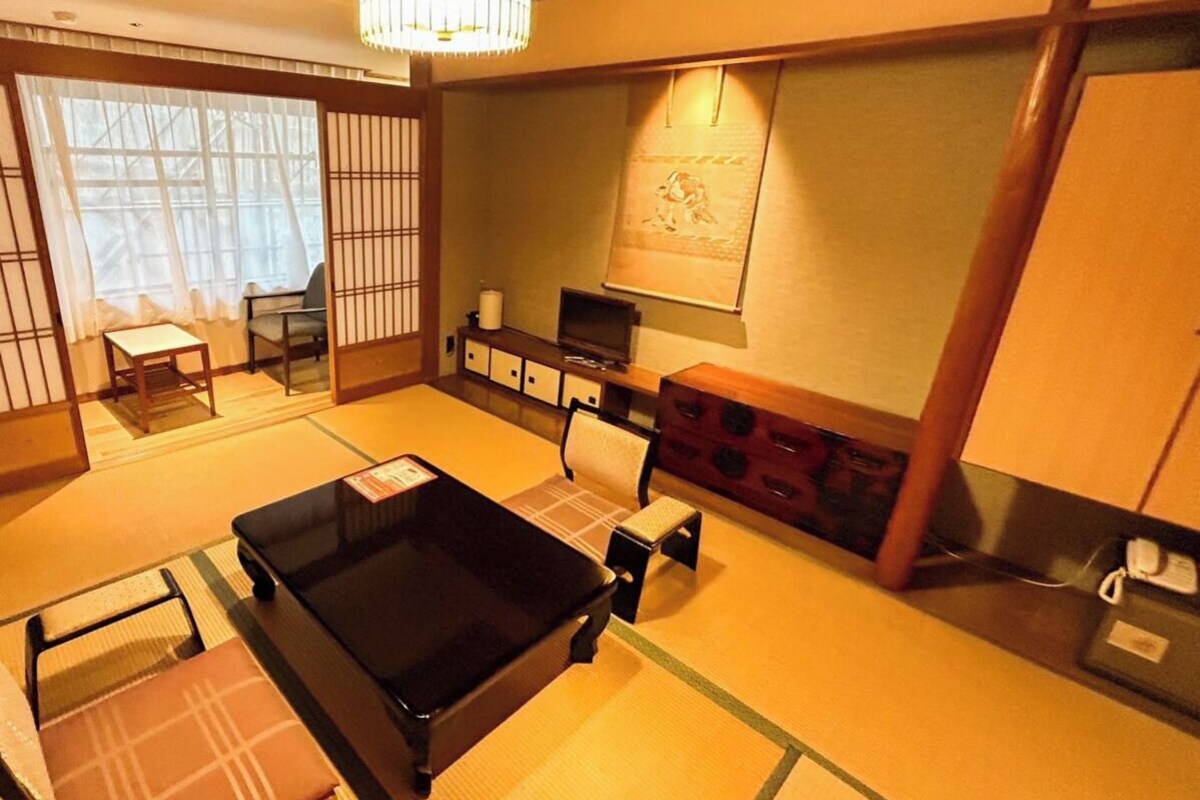 Una habitación tradicional japonesa con suelo de tatami, una mesa baja, un sofá, un televisor y un biombo decorativo.