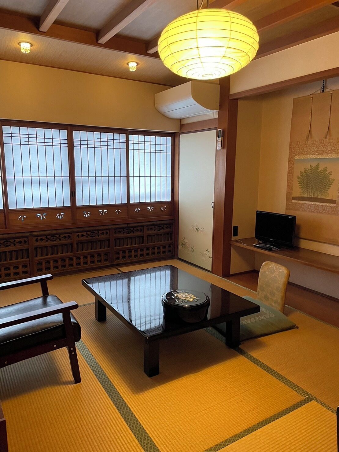 A traditional Japanese room with tatami flooring, a low table, a sofa, a television, and a sliding door.