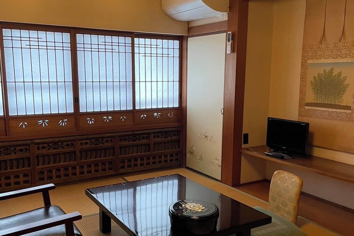 A traditional Japanese room with tatami flooring, a low table, a sofa, a television, and a sliding door.