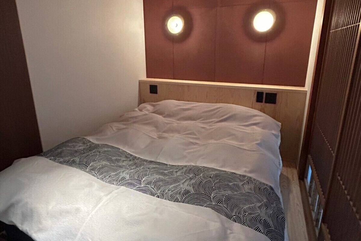 A hotel room with a bed, headboard with lights, and a wooden panel wall.