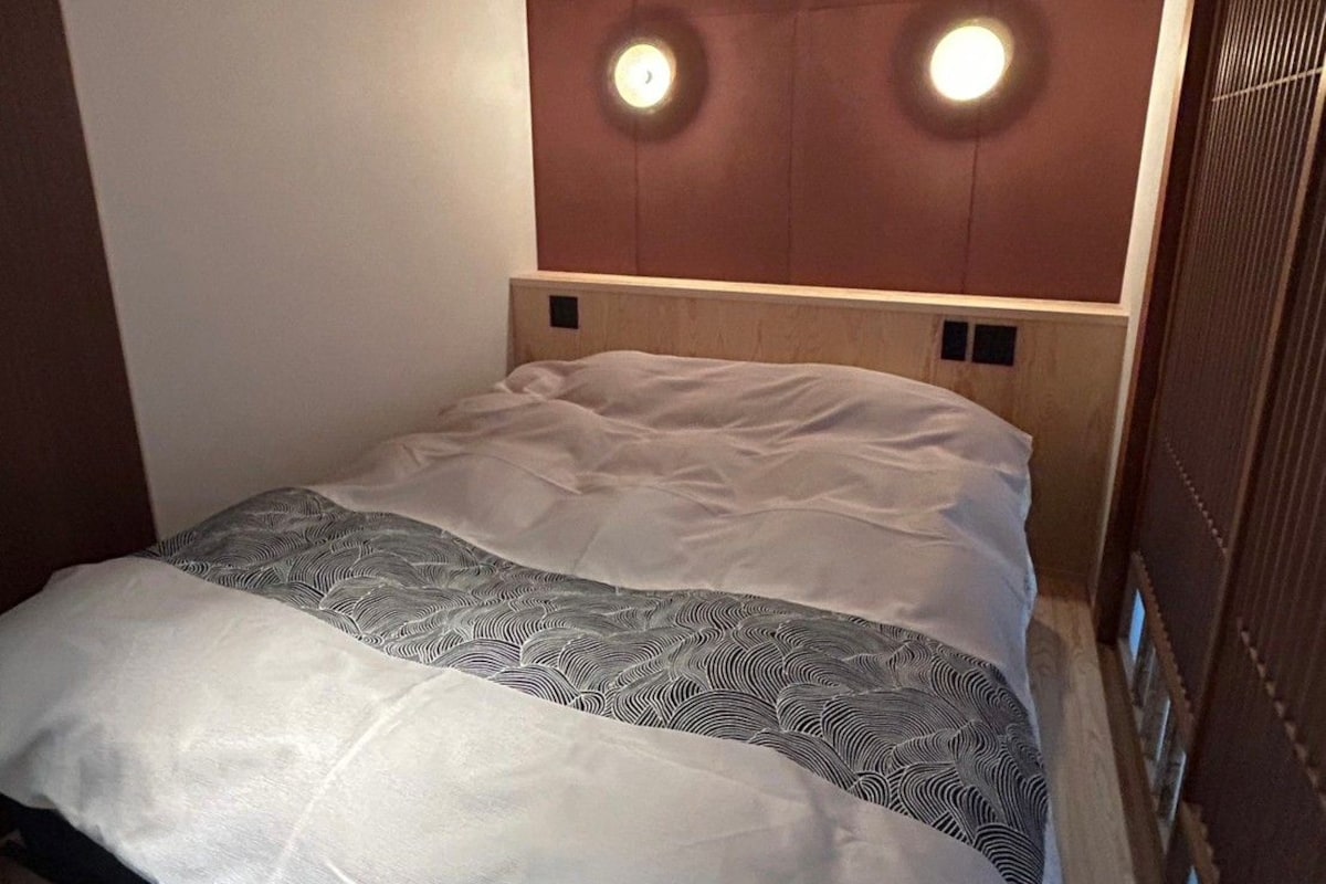 Habitación de hotel con cama, cabecera iluminada y panel de pared de madera.