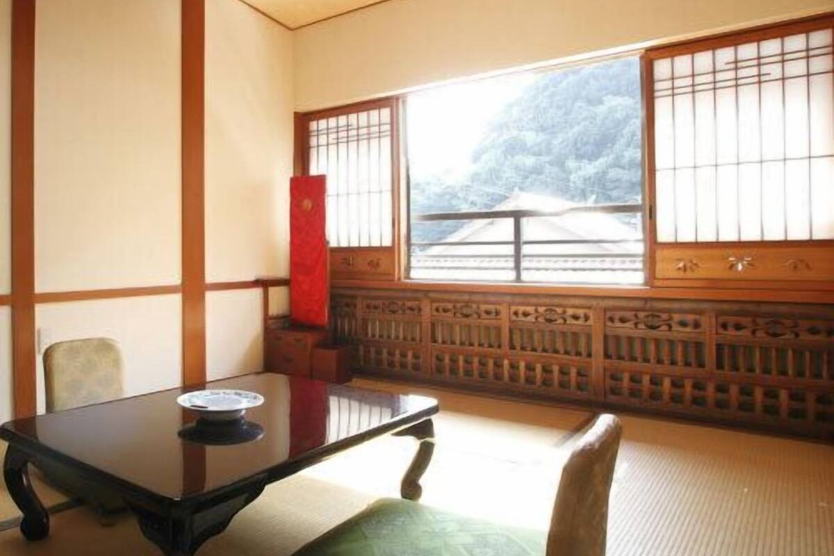 A traditional Japanese room with tatami flooring, a low table, a cushion, and a sliding door with a view of a mountainous landscape.