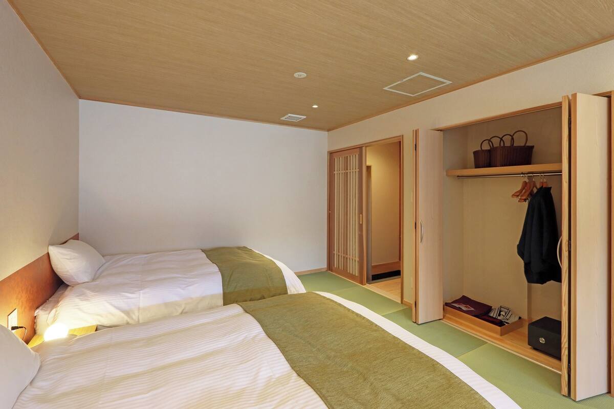 A bedroom with two beds, a wooden wardrobe, and a green mat.
