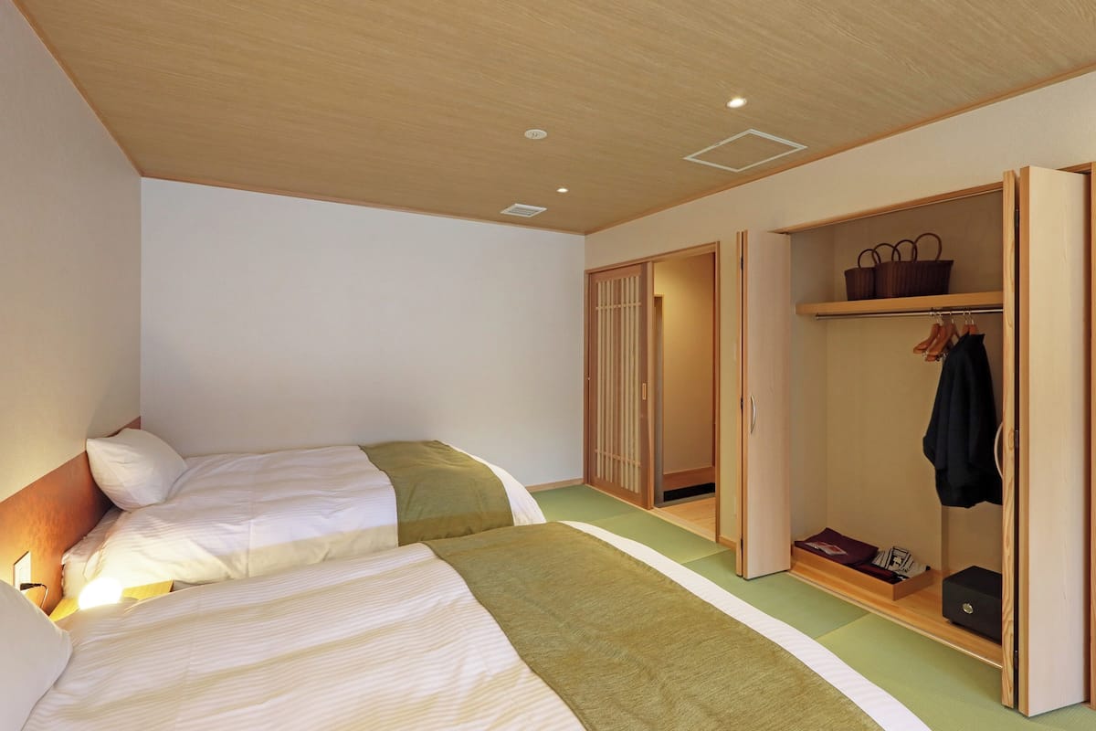 A bedroom with two beds, a wooden wardrobe, and a green mat.
