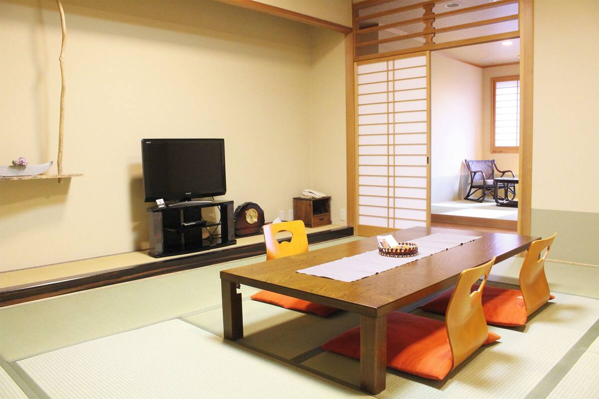 A traditional Japanese room with tatami flooring, a low table with cushions, a television, and a sliding door.