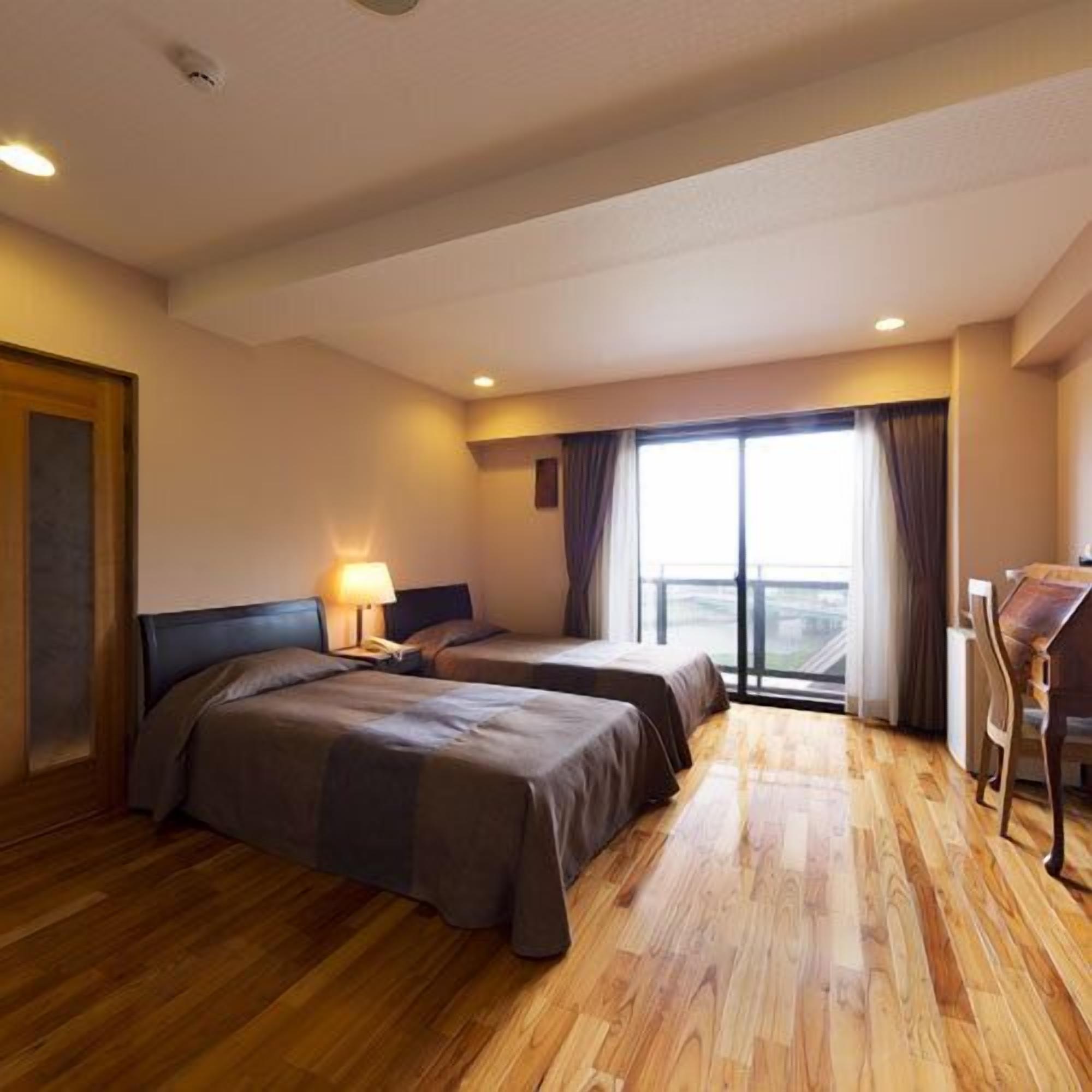 A hotel room with two beds, a desk, and a large window with curtains.