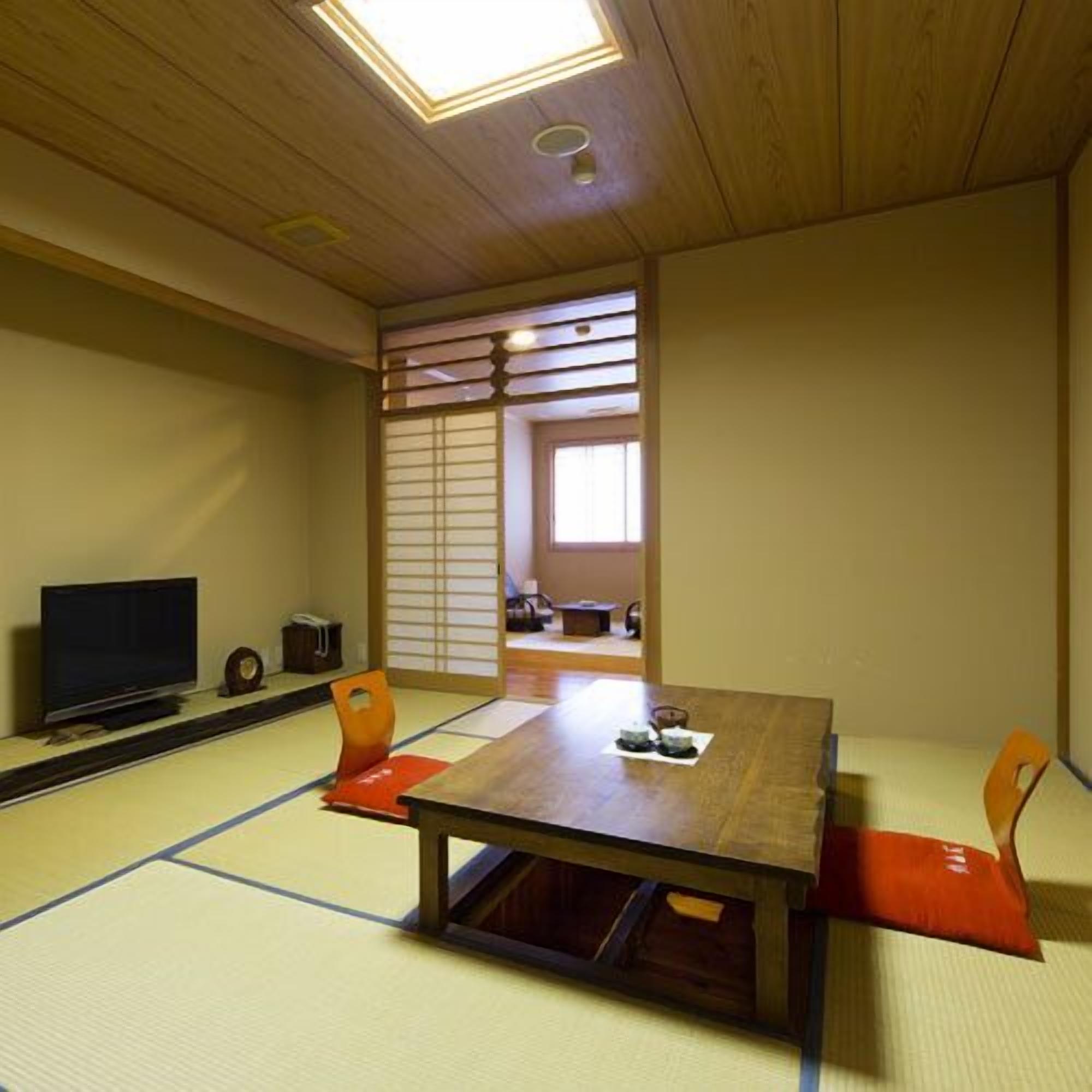 A tatami mat room with a low table, chairs, a television, and sliding doors.