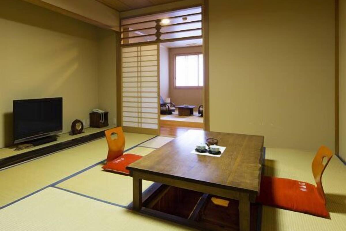 A tatami mat room with a low table, chairs, a television, and sliding doors.