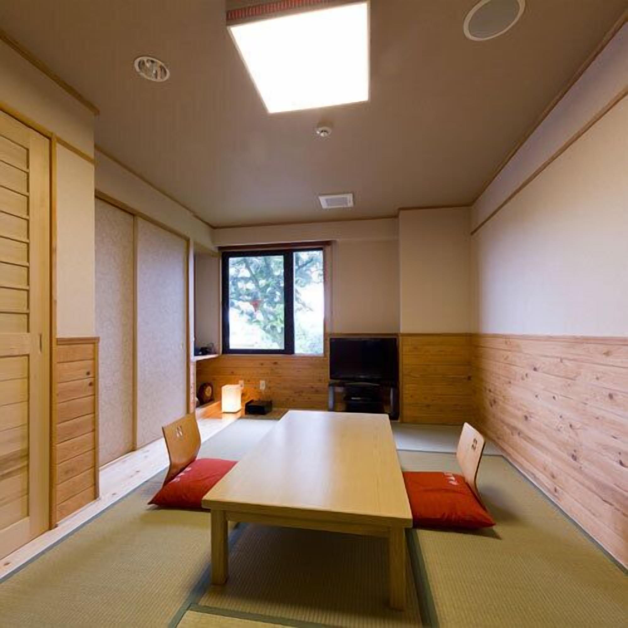 A room with a wooden table, chairs, a television, and a window.