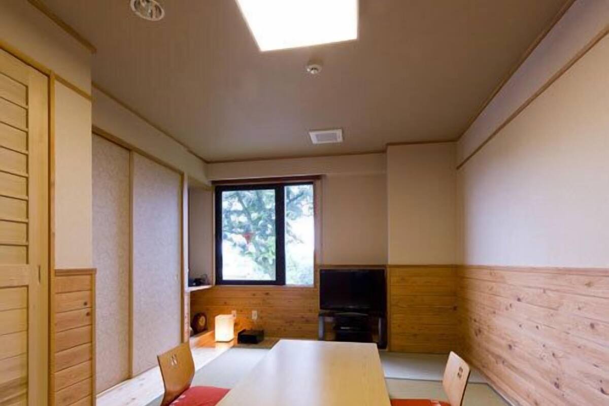 A room with a wooden table, chairs, a television, and a window.