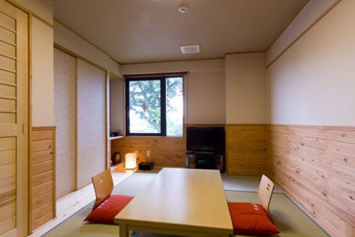 A room with a wooden table, chairs, a television, and a window.