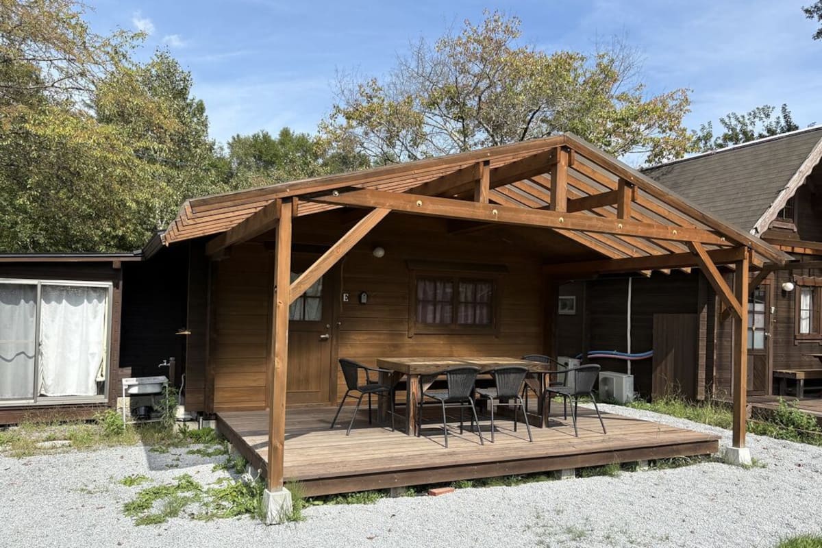 A wooden deck with a table and chairs, a covered area with a roof, and a small building with a window.