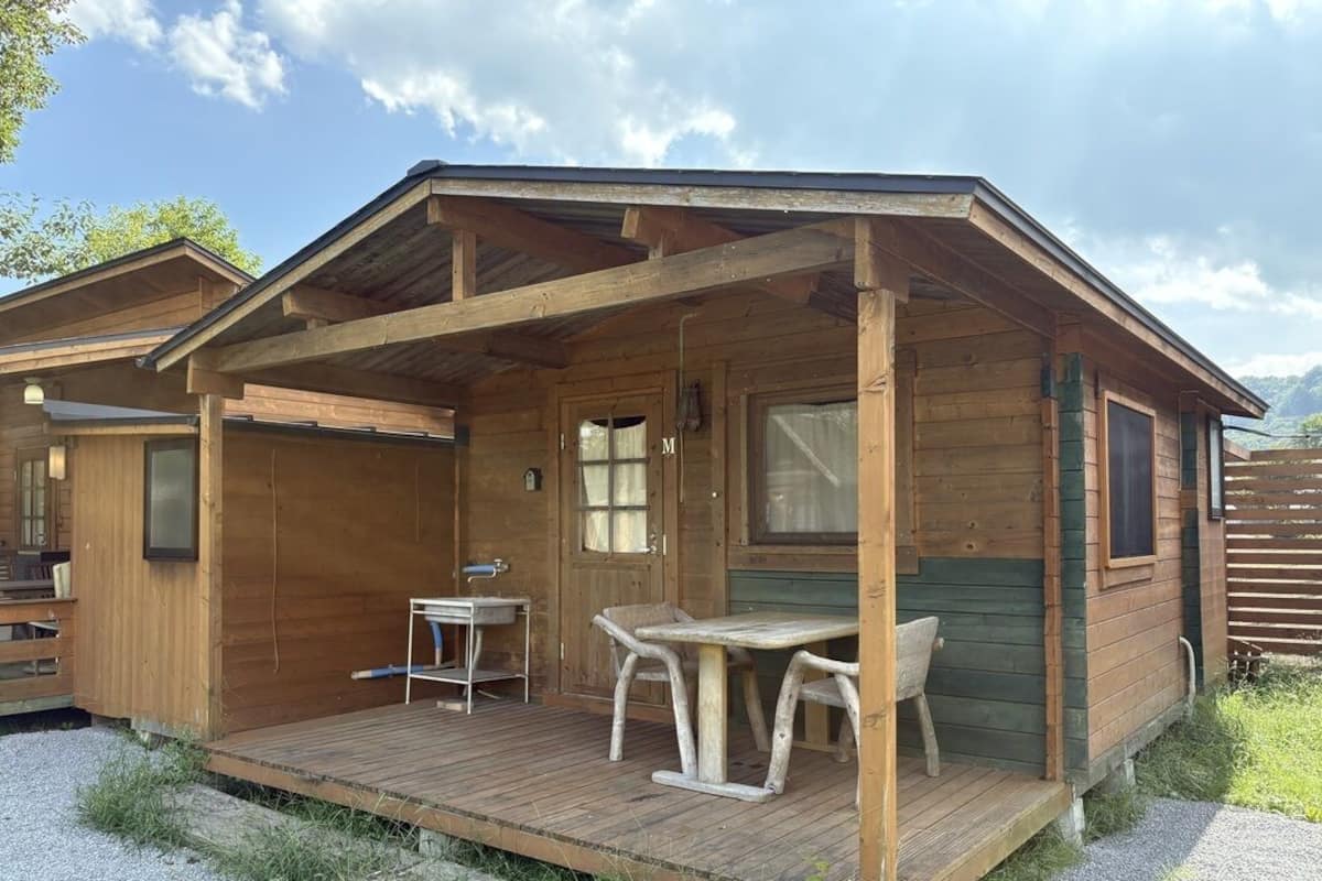 A wooden cabin with a porch, a table, and chairs.