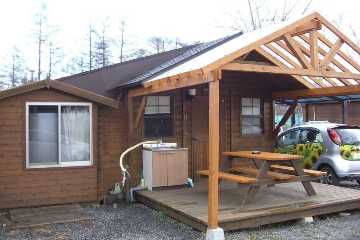 A wooden cabin with a covered porch, a sink, and a picnic table.